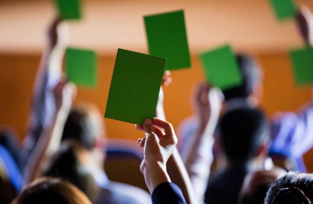 Participantes levantando tarjetas verdes durante una votación en un evento, simbolizando la aprobación o el apoyo a una propuesta.